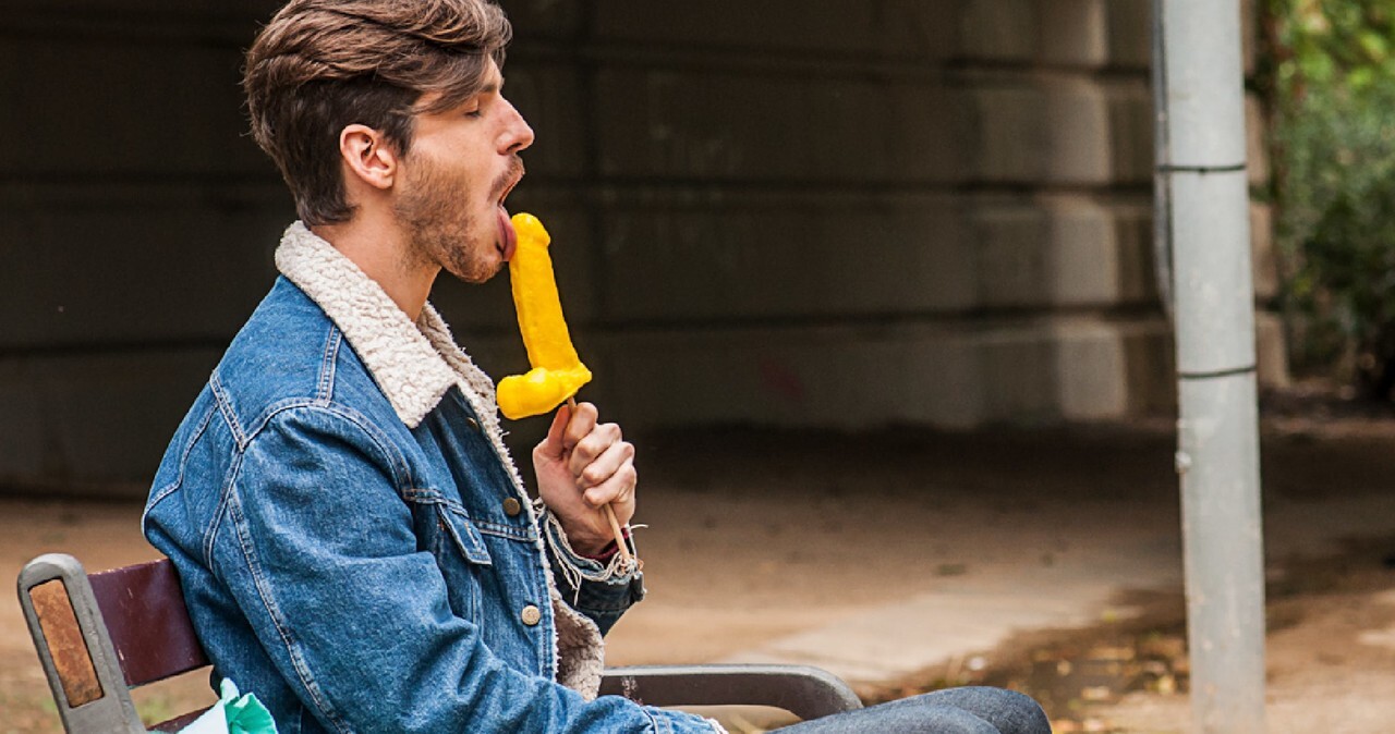 Gay brunette Victor A erotically sucks a sex toy lollipop on a public bench