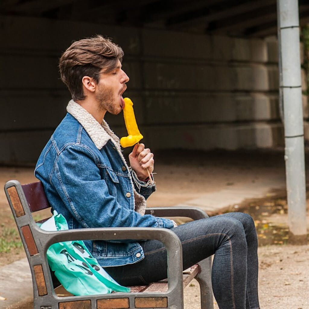 Gay brunette Victor A erotically sucks a sex toy lollipop on a public bench